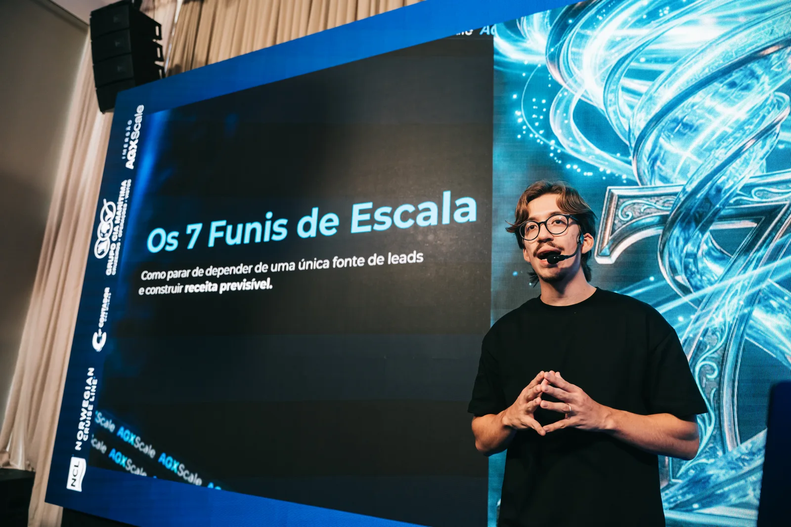 Arthur Pasetti no palco da Imersão AGX Scale 2026, com o telão Os 7 Funis de Escala